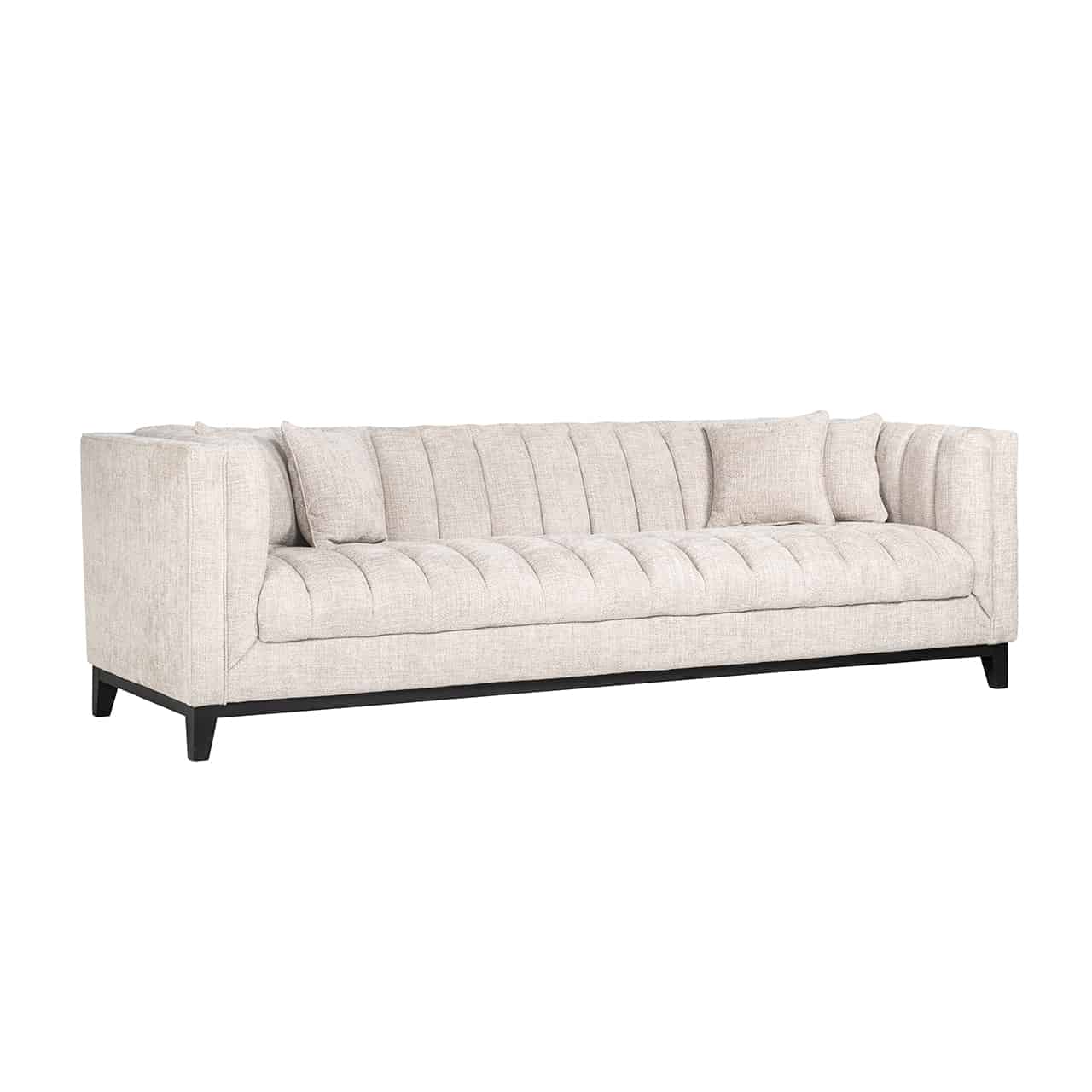 Großes, Beiges Sofa mit umlaufender Lehne auf einem schwarzen Gestell mit kurzen, eckigen, Beinen; die Sitzfläche und  die Seiten,- und Rückpolster sind mehrmals vertikal gesteppt; auf dem Sofa vier quadratische Kissen.